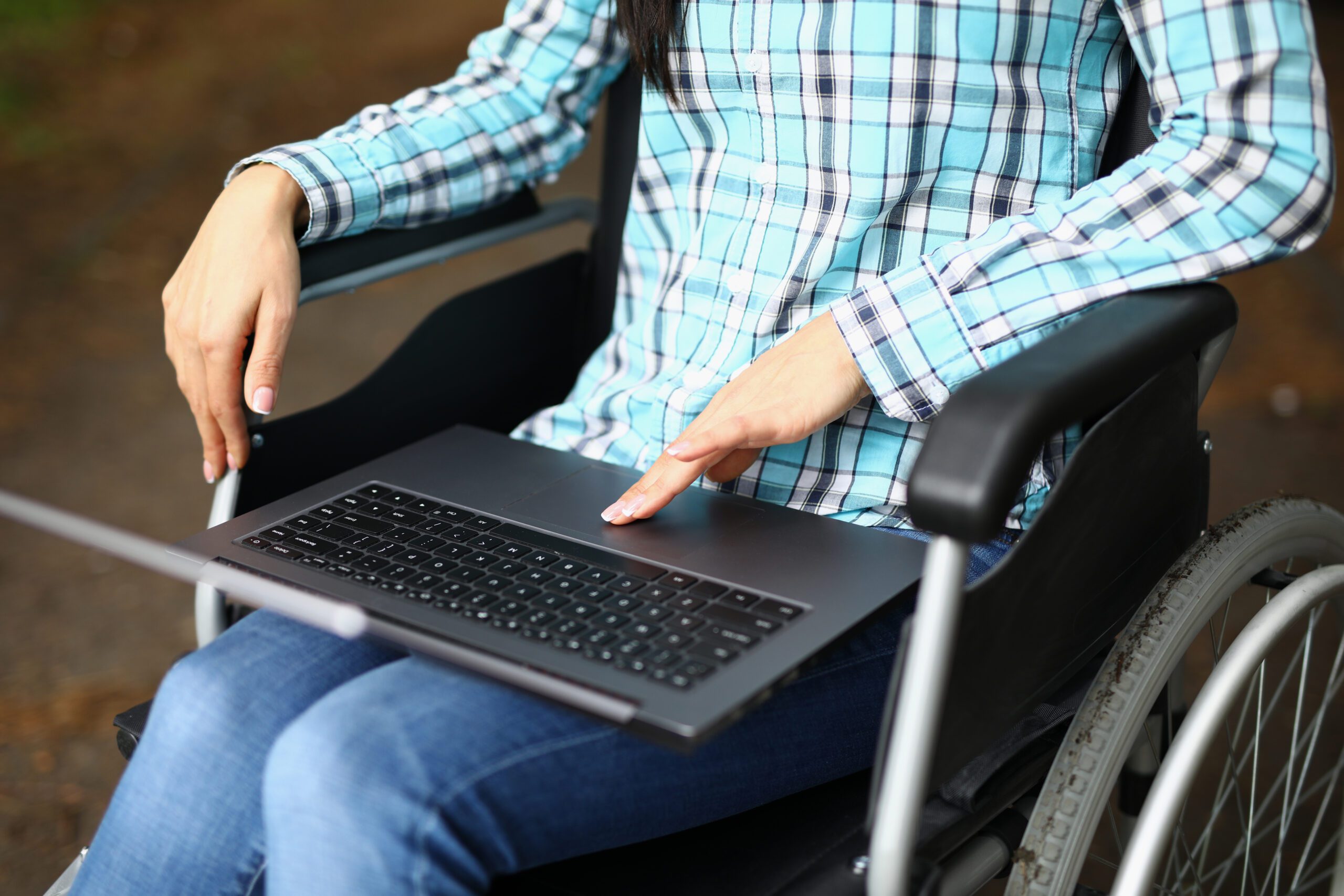 Person using a laptop while seated in a wheelchair outdoors